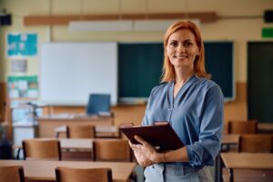 Happy,Primary,School,Teacher,Standing,In,The,Classroom,And,Looking